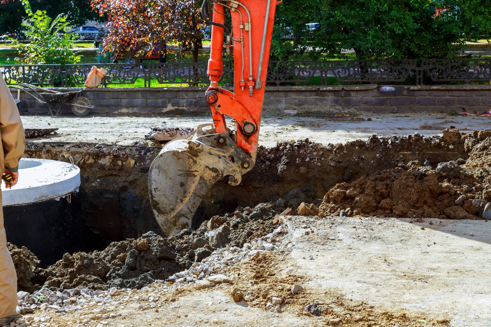 An orange excavator is working at a construction site, probably laying pipes or preparing the ground.