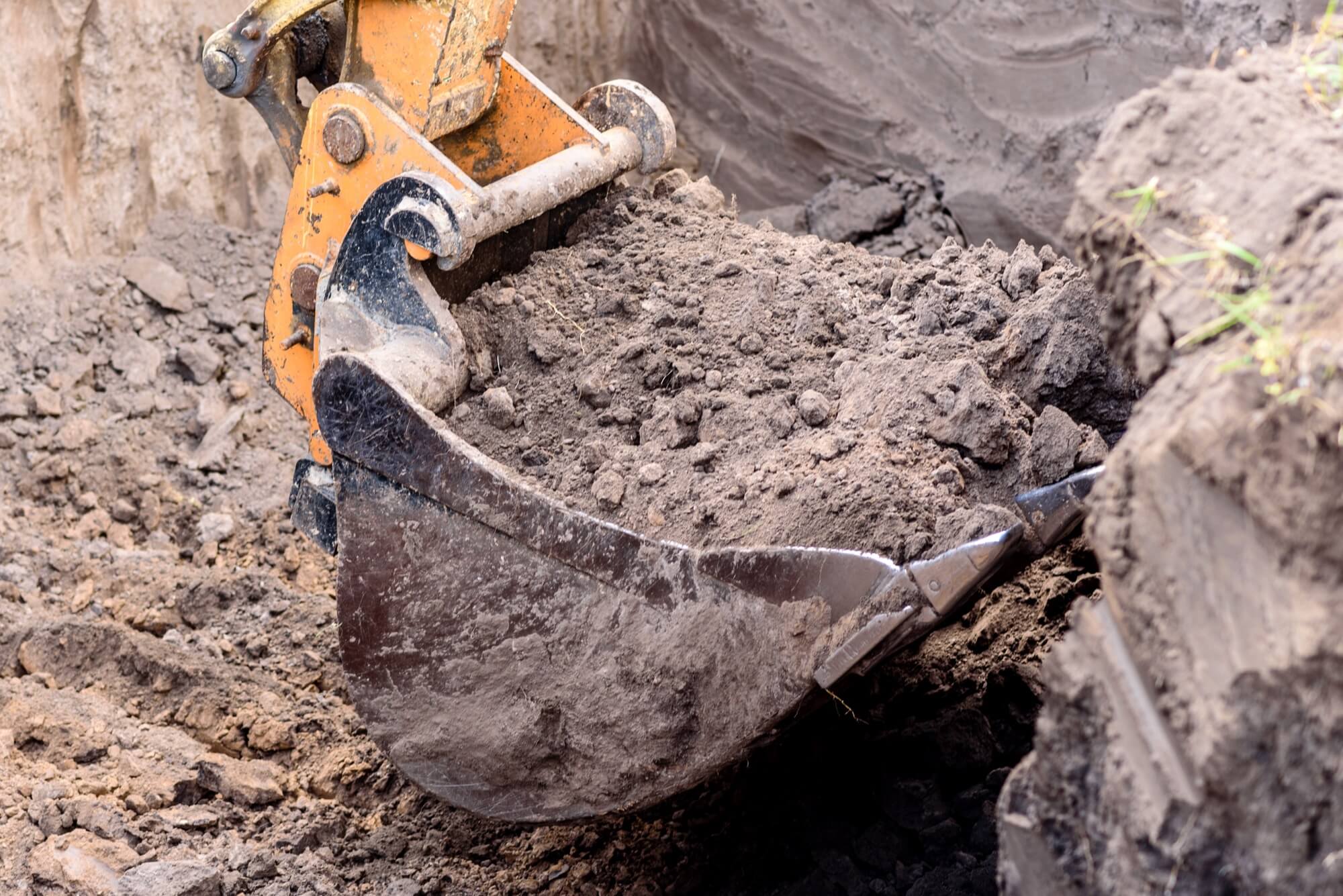 Close-up of an excavator bucket lifting earth masses during excavation work.
